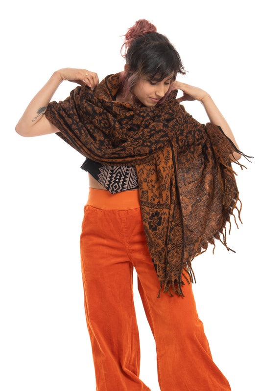 Black-Orange paisley shawl with fringe detailing, styled as an oversized wrap worn over orange corduroy pants with a geometric patterned belt.
